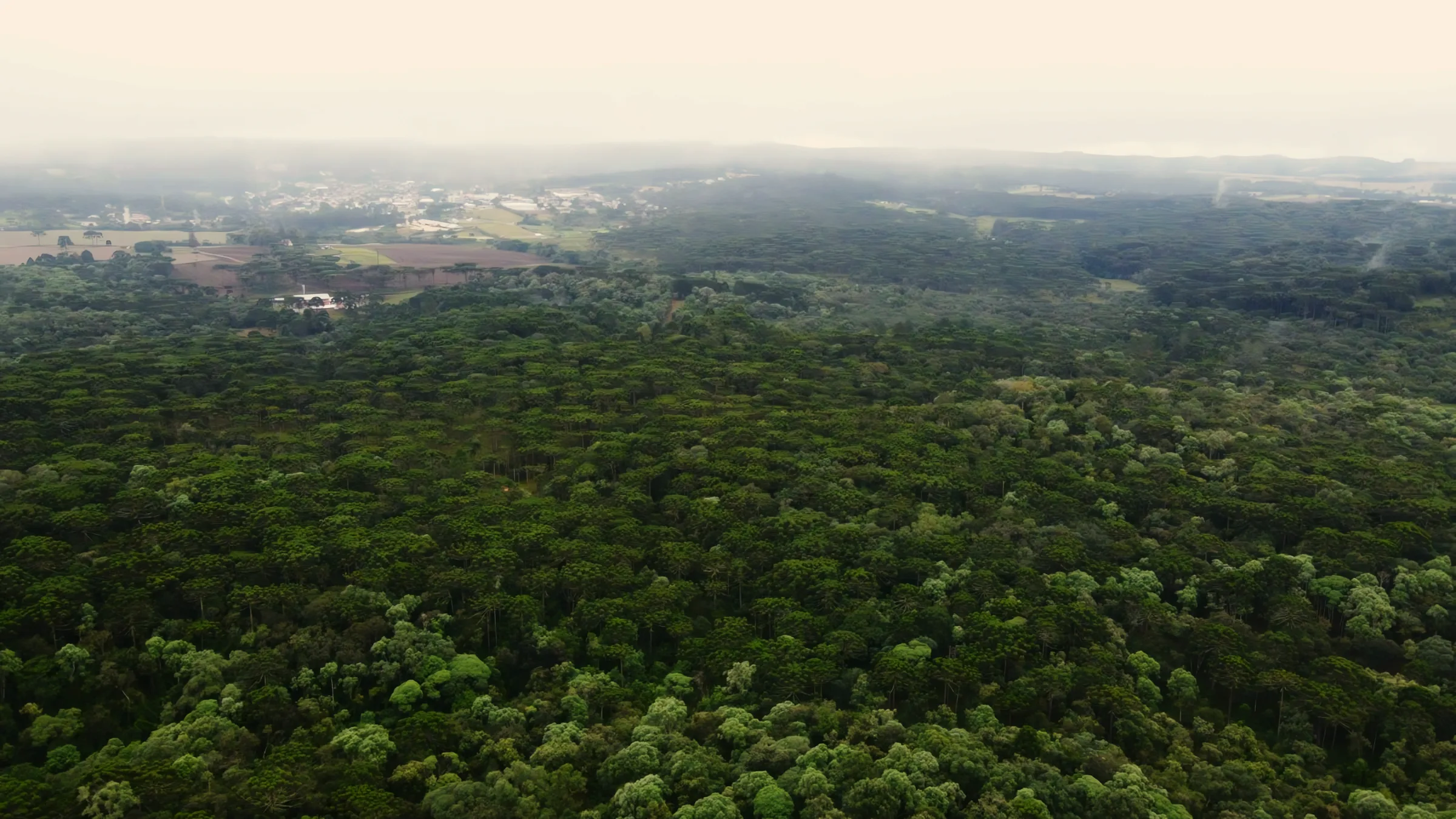 Imagem aérea de parte do empreendimento sob a neblina, com o centro da cidade ao fundo